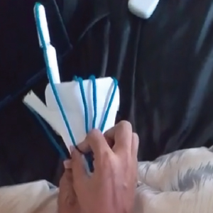 A paper prototype of a mechanical hand is shown, with strings attached to each finger. When the strings are pulled, the paper fingers lift, mimicking real finger movement. A person's hand is holding and pulling one of the strings to demonstrate the mechanism.